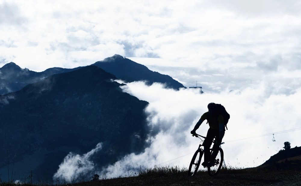 silhouette of a mountain biker riding on a trail with clouds and mountains in the background enjoying outdoor adventure and fitness