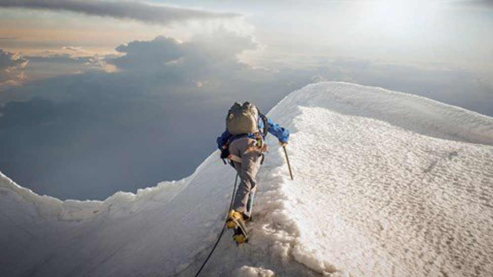 person climbing snowy mountain peak under cloudy sky adventurous climbing journey