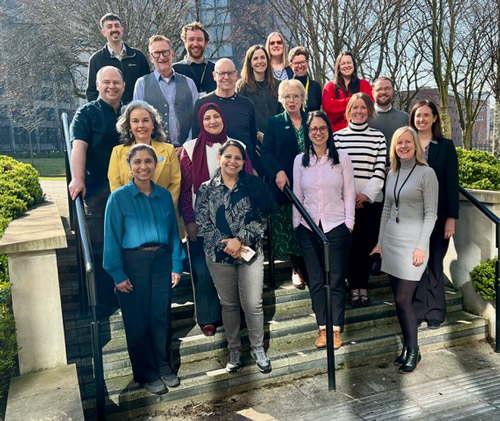 Group of diverse professionals standing on outdoor stairs with greenery in the background showcasing teamwork and collaboration in a workplace setting