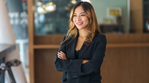 young businesswoman standing confidently in a modern office smiling wearing a black suit demonstrating leadership skills and professionalism